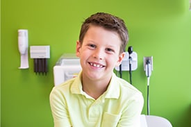 Grade-school-aged child sitting in an exam room at the doctor's office, smiling at the camera