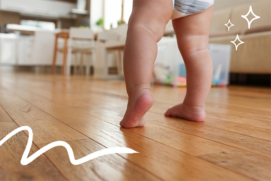 15-month-old toddler practices walking barefoot across a wooden floor.