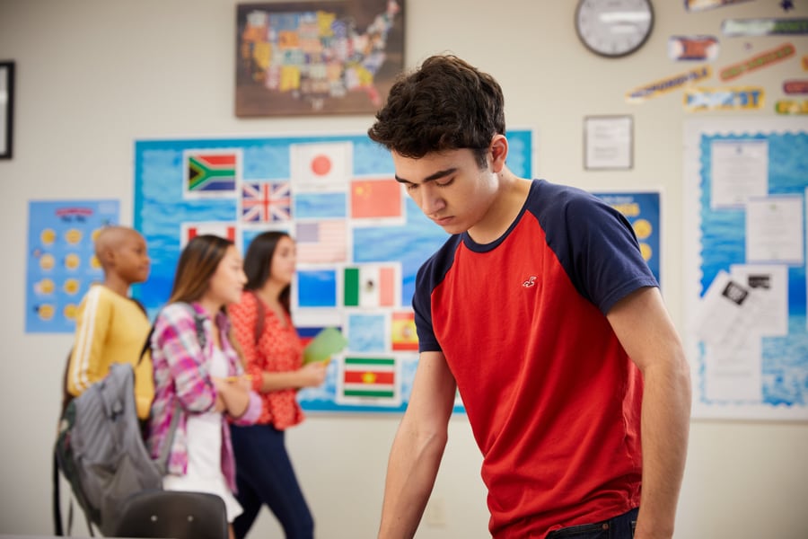 Teenage boy looks distracted and upset at school as classmates walk by.