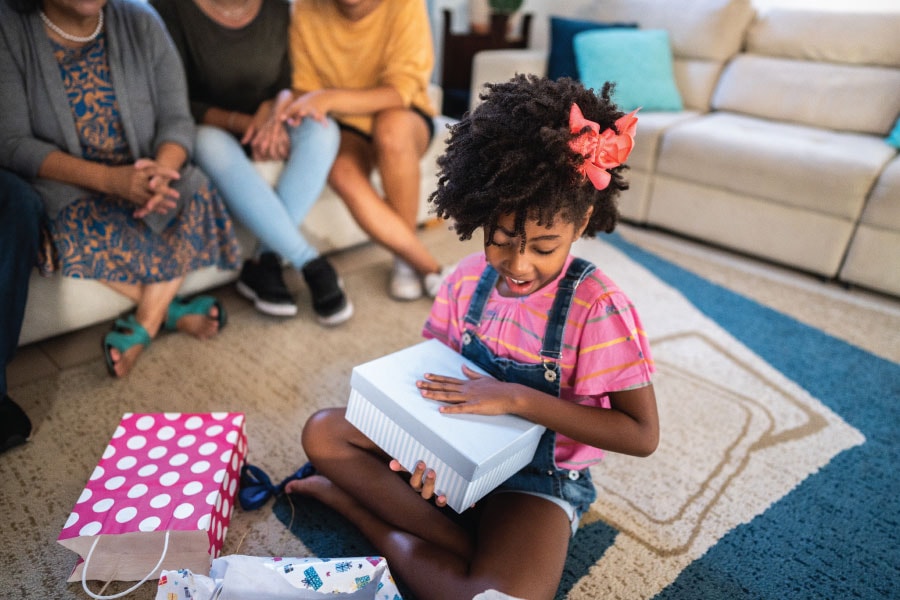 Young girl opens a present while sitting on the floor.