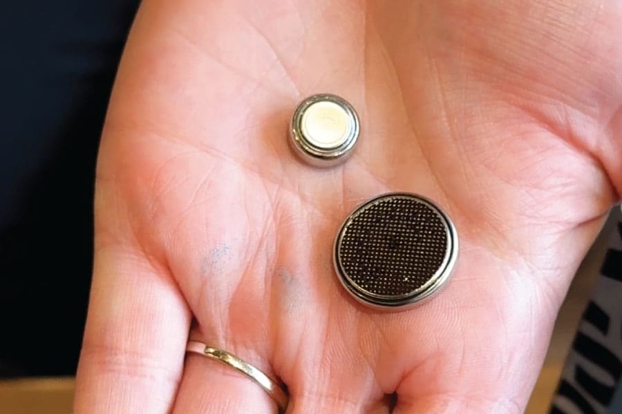 Two different sized button batteries in the palm of a hand to show how small they are.